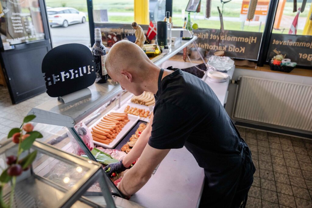 Slagter arbejder ved køledisk fyldt med pølser og friske varer.