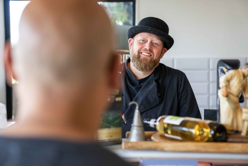 Slagtermester i sort uniform med bowlerhat smiler til kunde.